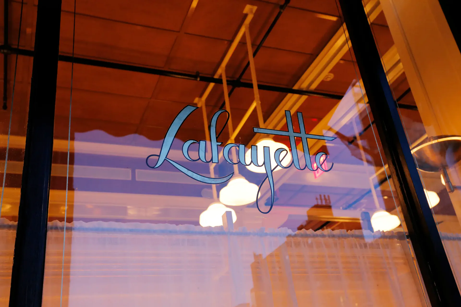 Neon signage reading 'Lunagluk' with cloud motifs illuminated in blue and white inside a storefront window at dusk, designed by Hervé Descottes.