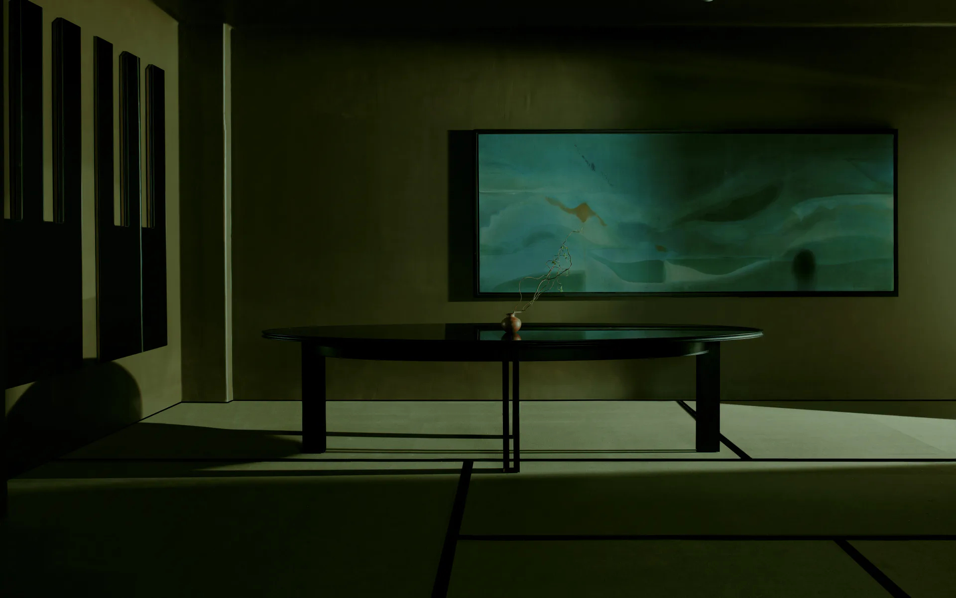 Minimalist interior space with dark furniture and teal-lit wall display, designed by Mark Grattan.