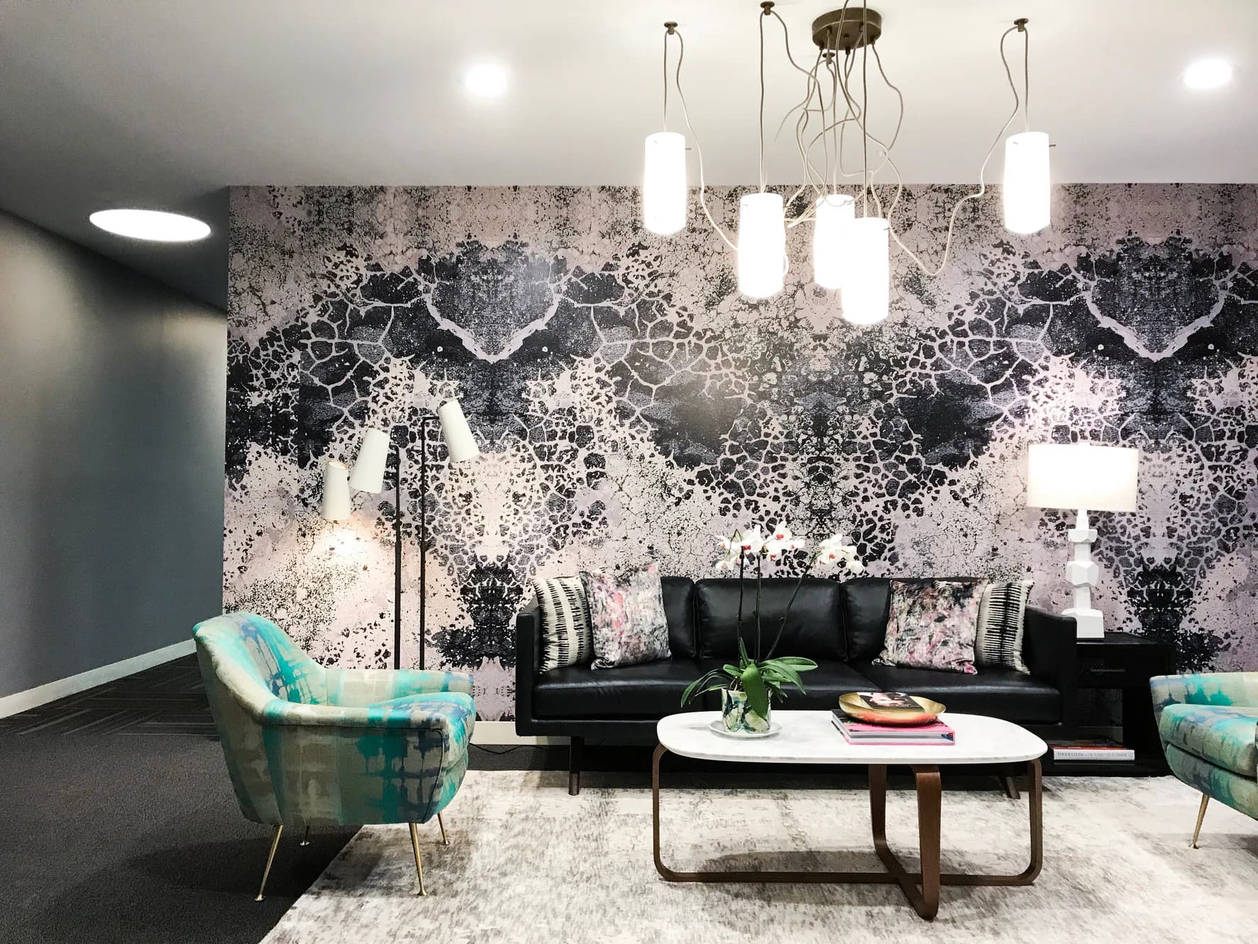 Modern lounge with black leather sofa, turquoise accent chairs, and striking abstract black-and-white patterned wallcovering by Apartment 48.