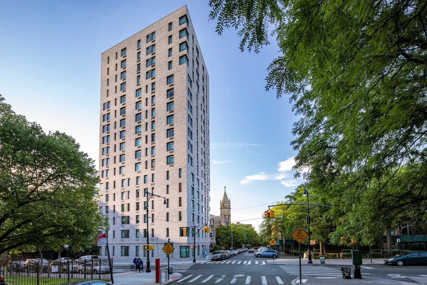 Tall residential building with cream and blue facade situated on urban corner plaza with trees and crosswalk by Marvel.